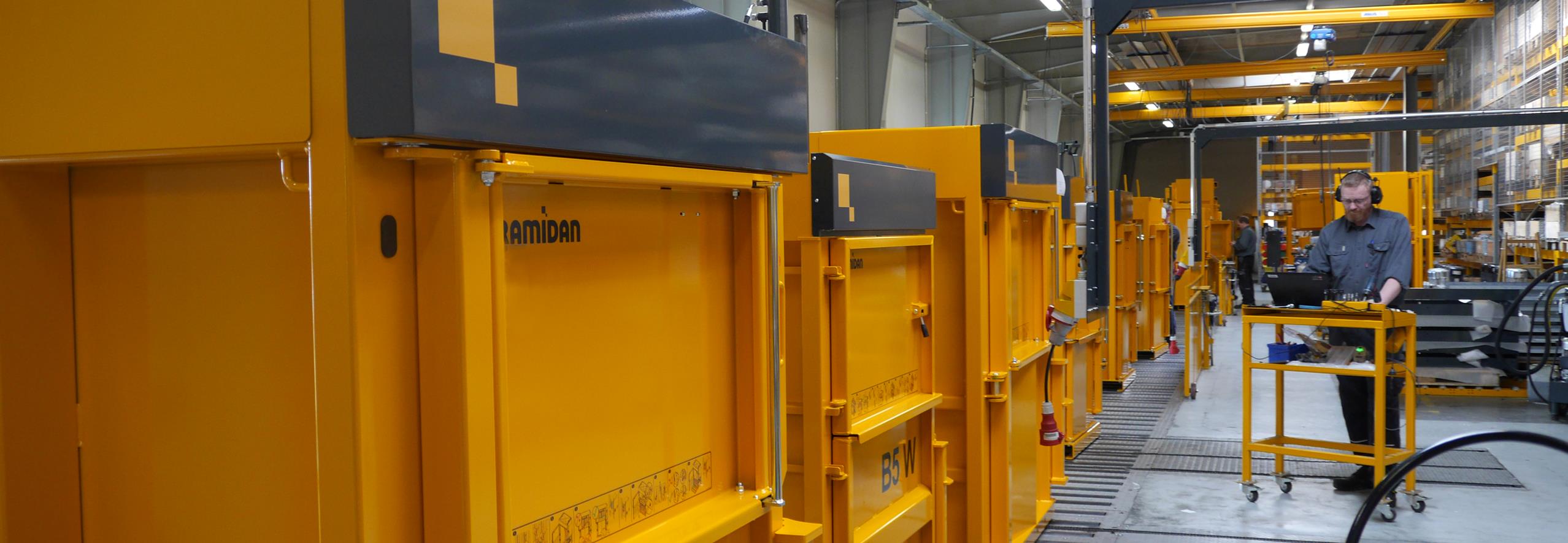Production line filled with yellow balers and man with earmuffs