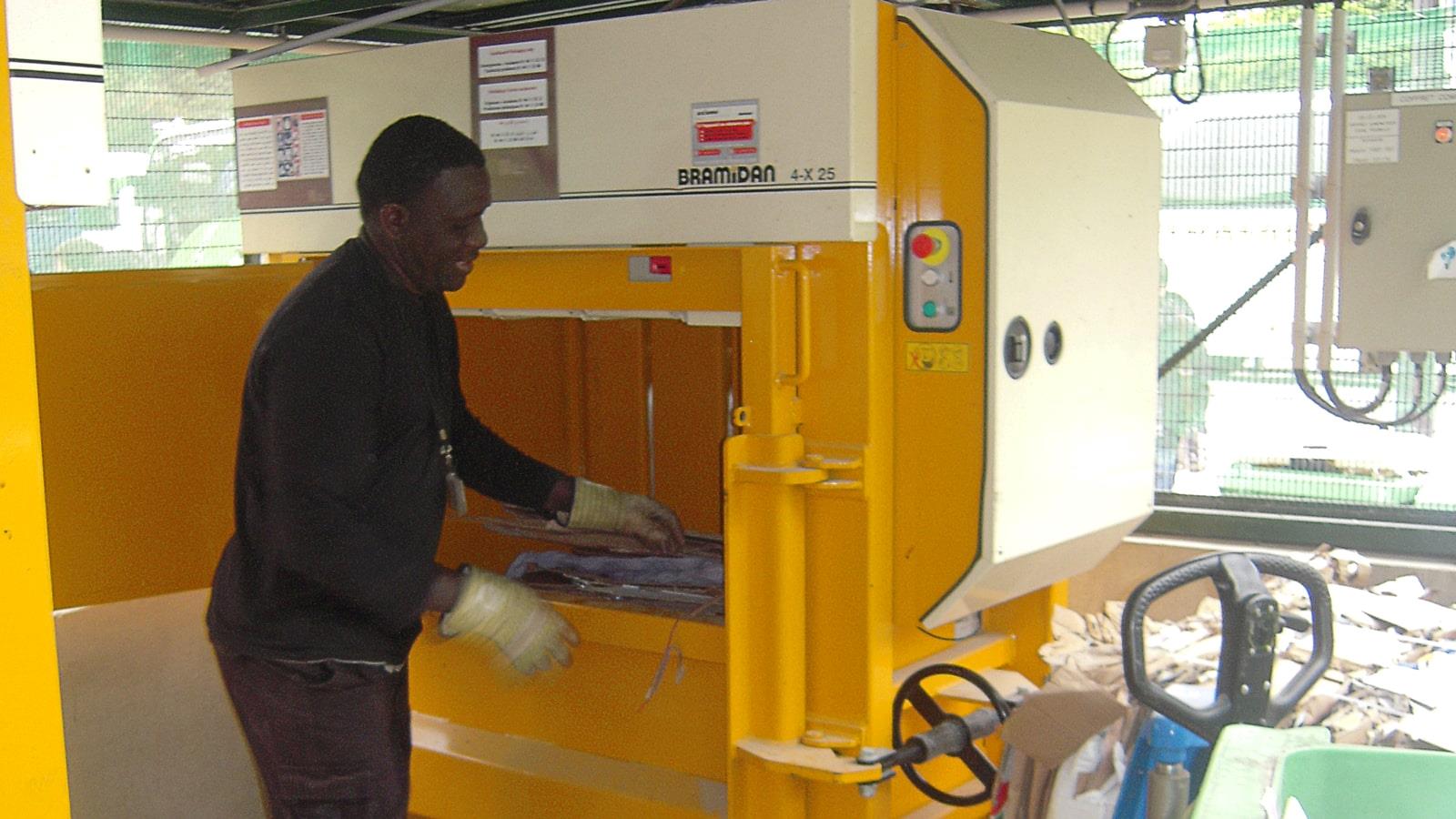 Employee with gloves fills cardboard waste into baler