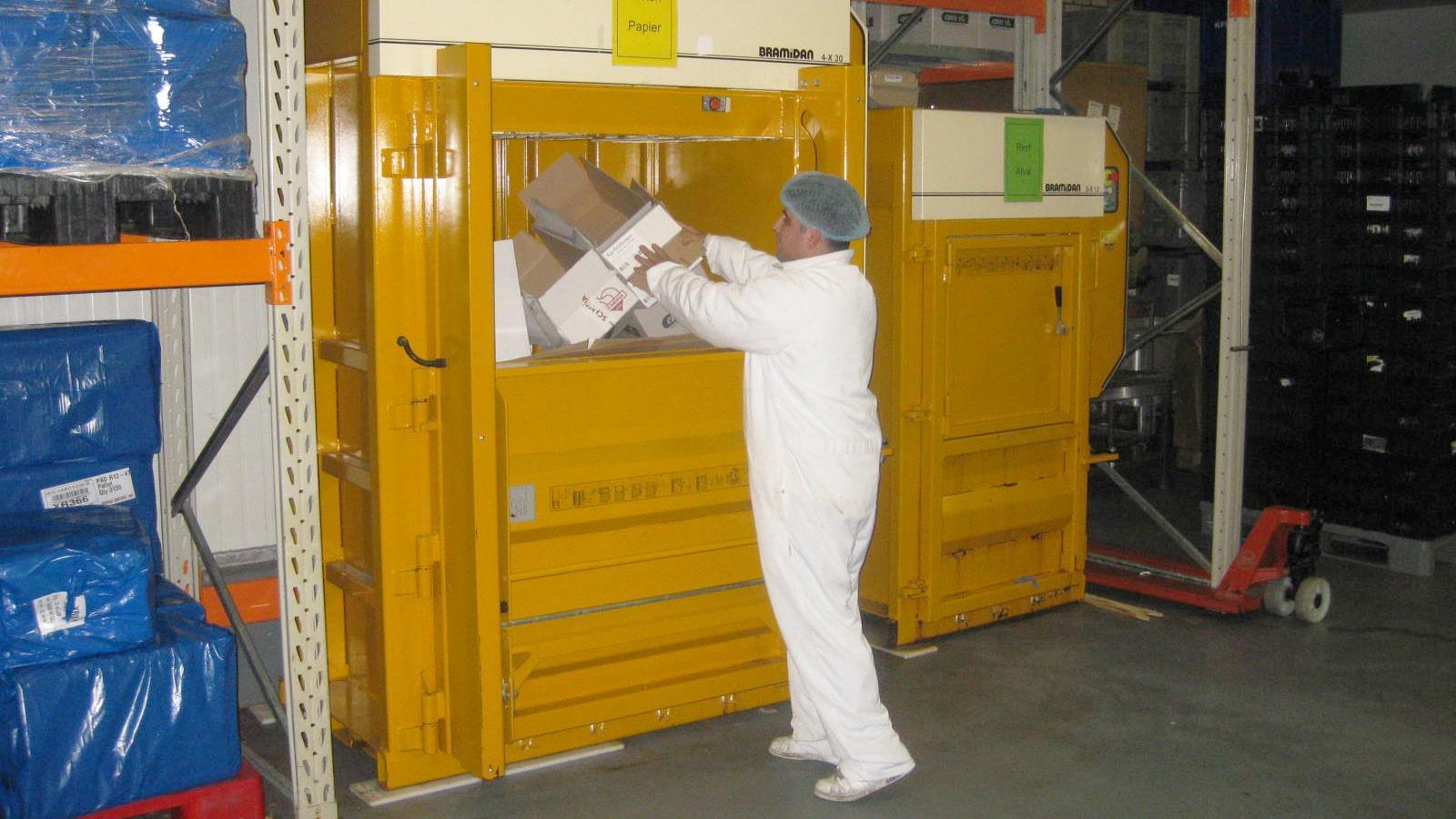 Man in white worksuit compacting cardboard in Bramidan baler